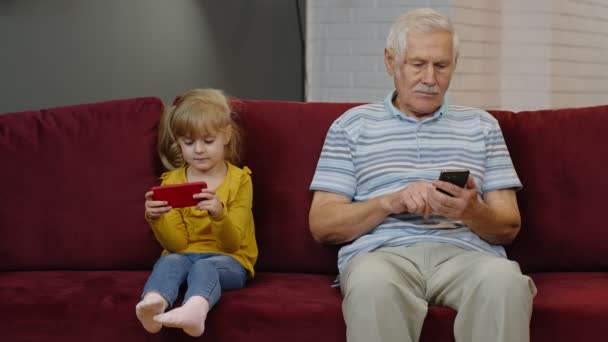 Abuelo mayor con nieta niña utilizando el teléfono móvil digital, jugando juegos en casa — Vídeos de Stock