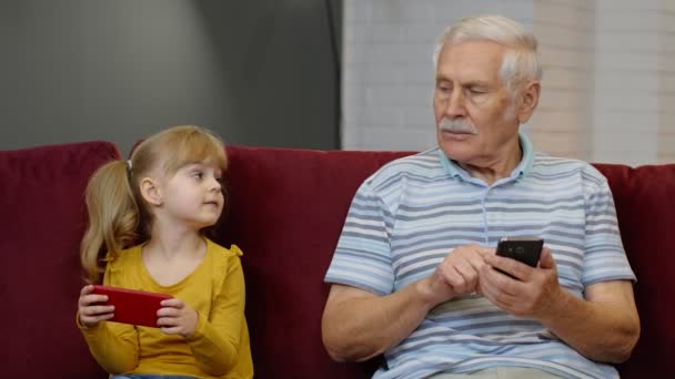 Abuelo mayor con nieta niña utilizando el teléfono móvil digital, jugando juegos en casa — Vídeos de Stock