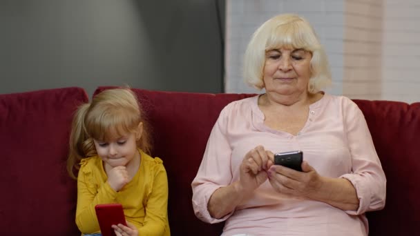 Büyükanne ve torunu dijital cep telefonu kullanıyor, evde oyun oynuyorlar. — Stok video