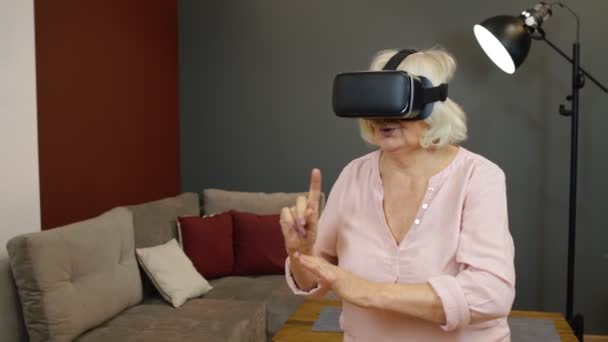 Femme grand-mère senior dans des lunettes de casque virtuel regarder incroyable vidéo 3D dans le casque VR à la maison — Video