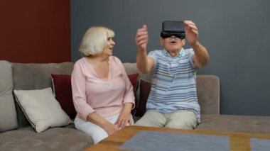 VR kulaklıklı büyükbaba ve büyükanne oyun oynuyorlar, sanal gerçeklik 3D video izliyorlar.