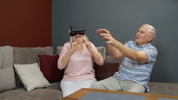 Seniorin spielt Spiel mit Virtual-Reality-Headset-Brille, Mann lacht bei ihrer Aktion zu Hause — Stockvideo
