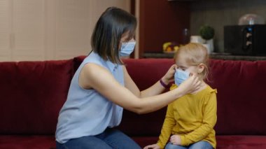 Annem evde küçük hasta kızını koruyucu bir tıbbi maske takıyor. Coronavirus karantina kilidi