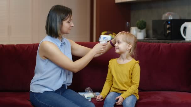 Madre misura la temperatura con termometro digitale contactless di sua figlia malata bambino a casa — Video Stock