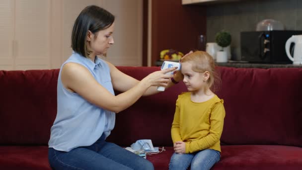 Matka měří teplotu bezkontaktním digitálním teploměrem nemocného dítěte doma — Stock video