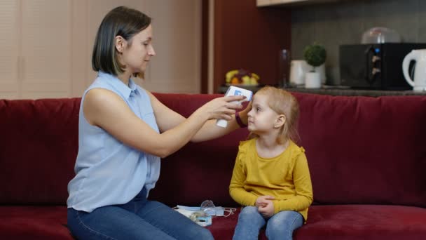 Mor mäter temperaturen med kontaktlös digital termometer av hennes söta dotter barn hemma — Stockvideo