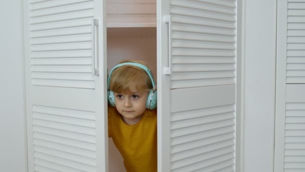 Liten barn flicka bär hörlurar lyssna på musik och lustigt dans nära garderob hemma — Stockvideo