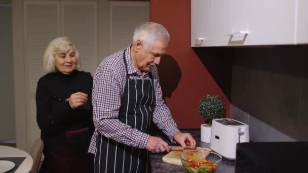 Pareja madura enamorada haciendo la cena. Mujer anciana abrazando desde atrás marido cocina comida en la cocina — Vídeos de Stock