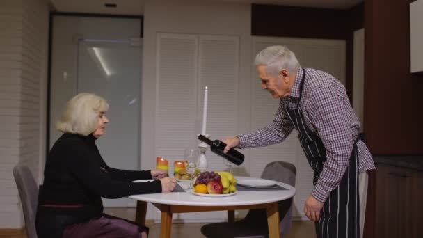 上了年纪的夫妇在厨房吃浪漫晚餐时，一边喝酒一边吃饭，玩得很开心 — 图库视频影像