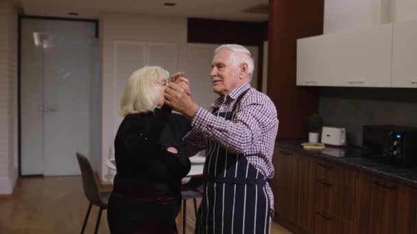 Старші закохані мають романтичний вечір, танцюють разом на кухні, святкуючи річницю — стокове відео