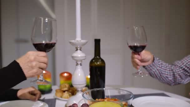 Крупним планом клінкінг червоних келихів вина під час романтичної вечері. Щасливі веселі старші літні пари — стокове відео