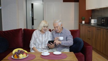 Yaşlı çiftin evde dijital tablet bilgisayar kullanması ve konuşması. İnternet alışverişi