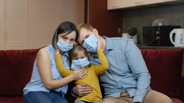 Coronavirus karantina kilidi. Anne, baba ve kız tıbbi maskeli evde yüzleri var.