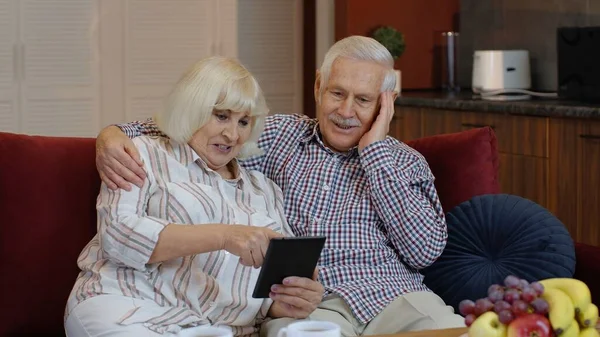 Senior pareja de pensionistas con tableta digital ordenador PC en casa. Descansando en el sofá en acogedora sala de estar — Foto de Stock