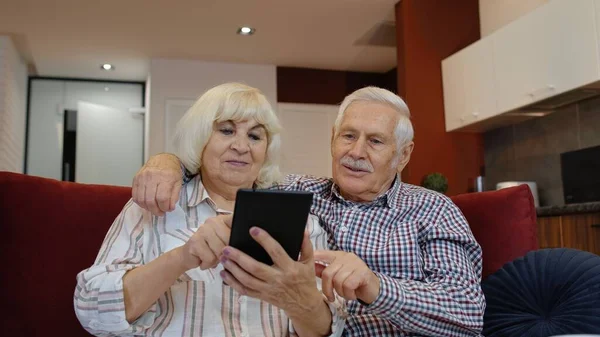 Ancianos abuelos de la vieja pareja hablando y usando tableta digital en casa. Compras por Internet — Foto de Stock