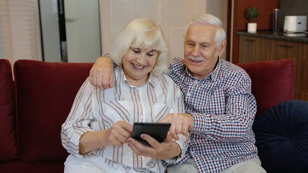 Senior pareja de pensionistas con tableta digital ordenador PC en casa. Descansando en el sofá en acogedora sala de estar — Foto de Stock