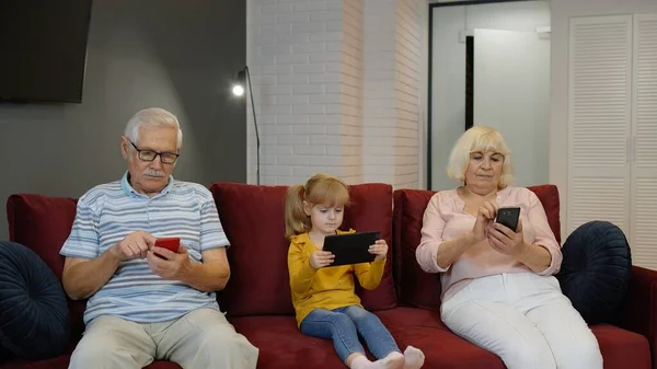 Senior couple grandparents with child girl granddaughter using digital tablet, mobile phone