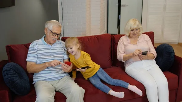Starsza para dziadków z wnuczkami dziewczynki korzystającymi z tabletu cyfrowego, telefonu komórkowego — Zdjęcie stockowe