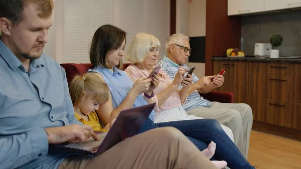 Устройства зависимых семьи использовать планшет, мобильный телефон сидеть на диване дома. Интернет-зависимость — стоковое фото