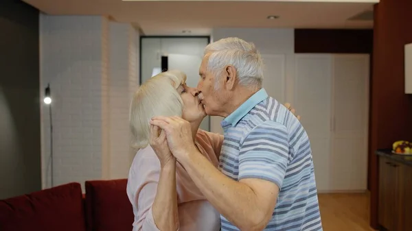 Happy mature senior couple dancing laughing in kitchen at home, celebrating anniversary, having fun