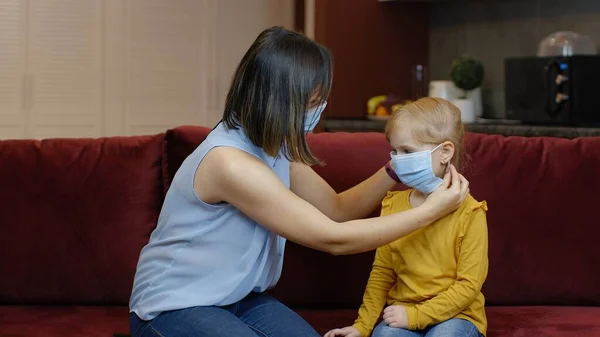 Mother puts on little sick daughter protective medical mask at home. Coronavirus quarantine lockdown