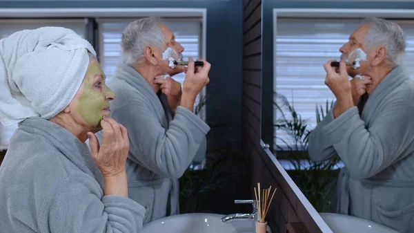 Old senior couple man and woman doing morning hygiene procedures and looking into a mirror — Stock Photo, Image