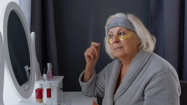 Anciana abuela anciana cuidando la piel cerca de los ojos y las arrugas, maquillándose en casa —  Fotos de Stock