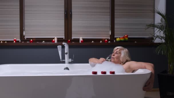 Aktive Seniorin liegt in warmem Bad mit Blasen und trinkt Champagner nach hartem Arbeitstag — Stockvideo