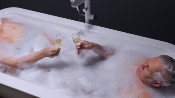 Seniorenpaar liegt in warmem Bad mit Blasen, genießt Entspannung, trinkt Champagner — Stockvideo