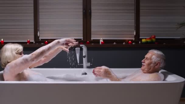 Aantrekkelijk senior paar liggend in warm bad met bubbels, genieten van ontspanning, spetterend water — Stockvideo