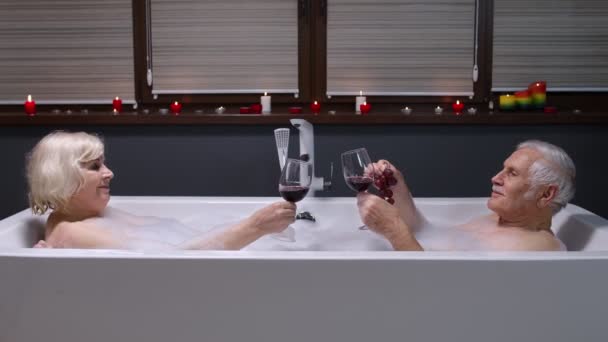 Senior couple grandfather and grandmother is taking foamy bath, drinking red wine in bathroom — Stock Video