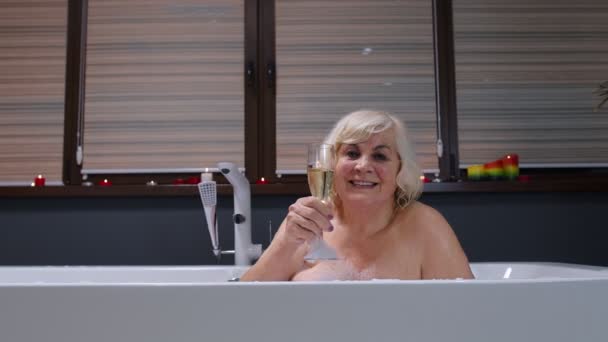 Anciana mujer mayor acostada en baño caliente con burbujas, disfrutando de la relajación, beber champán — Vídeos de Stock