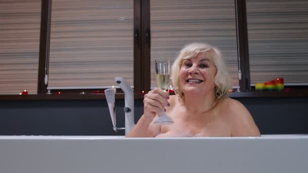 Actieve senior vrouw liggend in warm bad met bubbels, het drinken van champagne na harde werkdag — Stockvideo