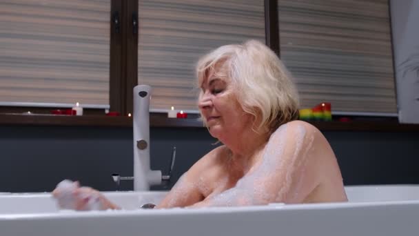 Mooie actieve oudere vrouw ligt in een warm bad met bubbels, genieten van ontspanning. Ouderen — Stockvideo