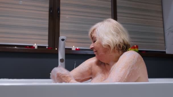 Sexy ältere blonde Frau Großmutter nimmt schäumendes Bad im Luxus-Badezimmer mit Kerzen — Stockvideo