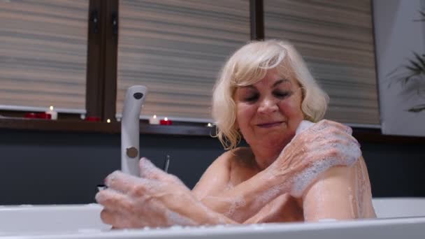バブルで暖かいお風呂に寝そべっている美しい活動的なシニア女性は、リラクゼーションを楽しんでいます。高齢者 — ストック動画