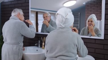 Üst düzey çift dişlerini fırçalıyor ve evdeki lüks banyoda aynaya bakıyor.