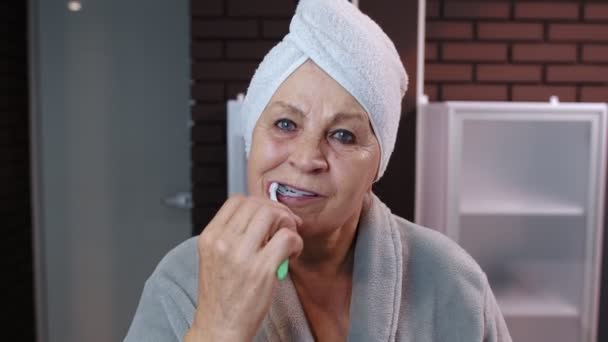 タオルブラッシング歯を持つシニア女性祖母と家でシャワーした後、鏡を見て — ストック動画