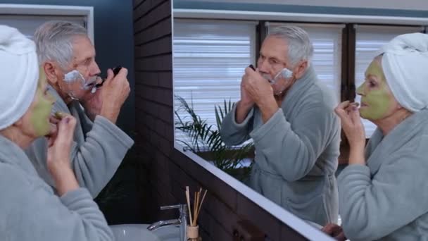 Мужчина и женщина пожилого возраста проводят утренние гигиенические процедуры и смотрят в зеркало — стоковое видео