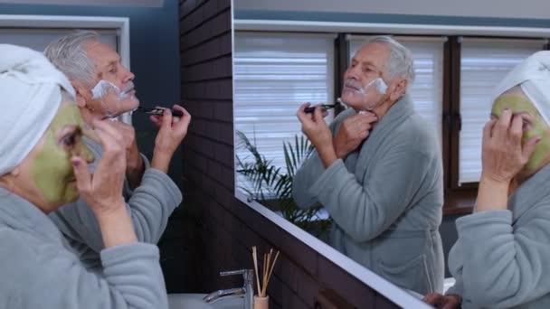 Avó sênior aplicando máscara facial e avô de barbear com lâmina de barbear manual no banheiro — Vídeo de Stock