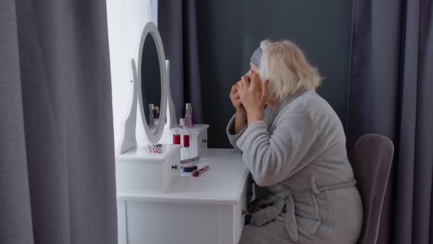 Viejo anciano abuela anciana aplicando parche antiarrugas en los ojos, maquillarse en casa — Vídeo de stock