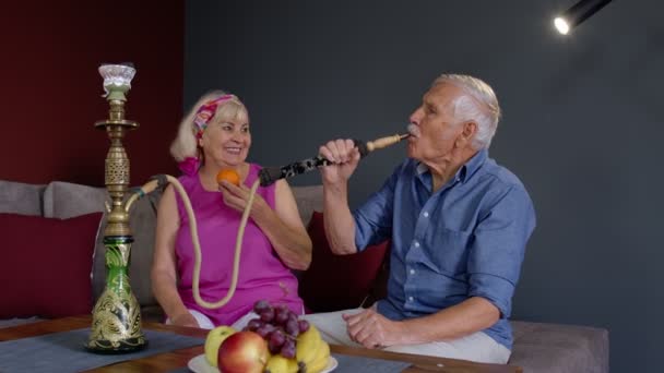 Pareja mayor fumando narguile comiendo frutas celebrando aniversario de jubilación en la sala de estar en casa — Vídeo de stock