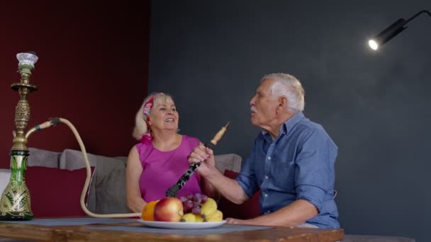 Pareja mayor fumando narguile comiendo frutas celebrando aniversario de jubilación en la sala de estar en casa — Vídeo de stock