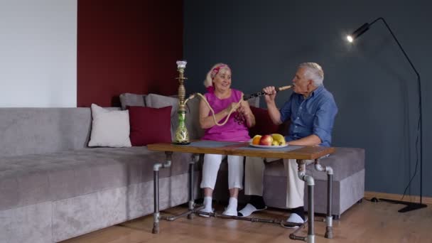 Elegante pareja de abuelos senior disfrutar de fumar narguile en casa, celebrando, divertirse juntos — Vídeos de Stock