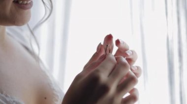 Gecelikli gelin, pencerenin yanında nişan yüzüğü olan duvak. Gülümseyerek yüzünü kapat. Düğün sabahı.