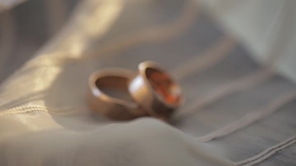 Dos anillos de boda de oro que yacen en la superficie blanco-gris del vestido que brilla con la luz de cerca macro — Vídeo de stock