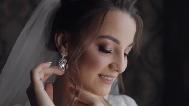 Η νύφη στο μπουντουάρ φοράει σκουλαρίκια. Πρωινές ετοιμασίες γάμου. Γυναίκα με νυχτικό και πέπλο — Αρχείο Βίντεο