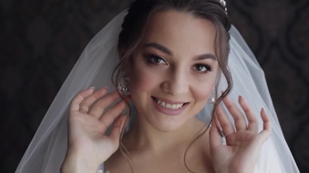 Sposa in abito boudoir si mette orecchini. Preparativi per il matrimonio. Donna in abito da notte e velo — Video Stock