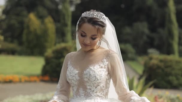 Mooie en mooie bruid in trouwjurk en sluier in het park wachtend op bruidegom. Langzame beweging — Stockvideo