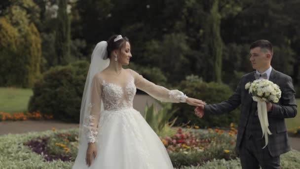 Молодожёны. Кавказский жених с невестой, гуляющей в парке. Свадебная пара. Мужчина и женщина влюблены — стоковое видео